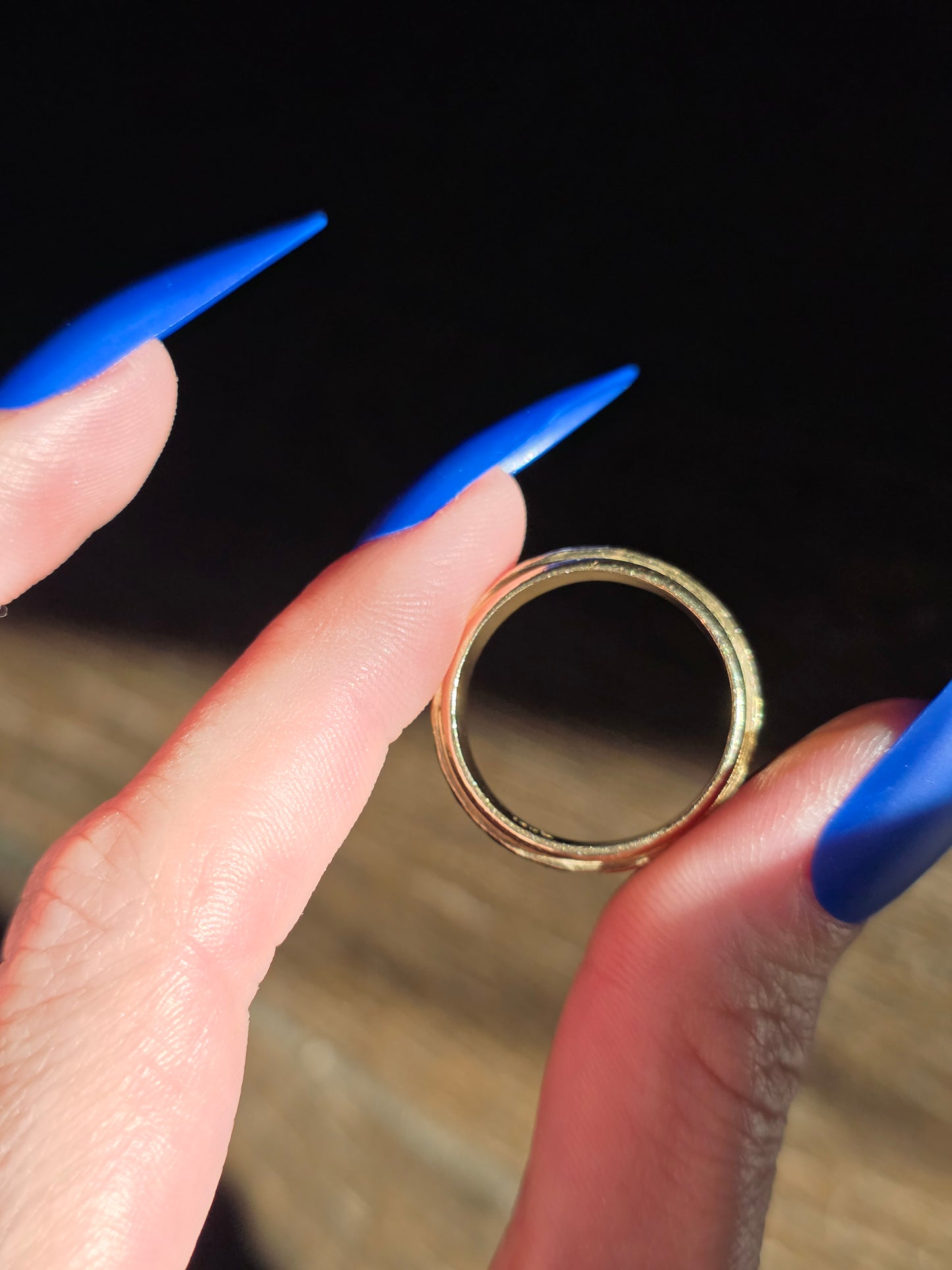 Gold ring held between two fingers with blue nail polish on a blurred background
