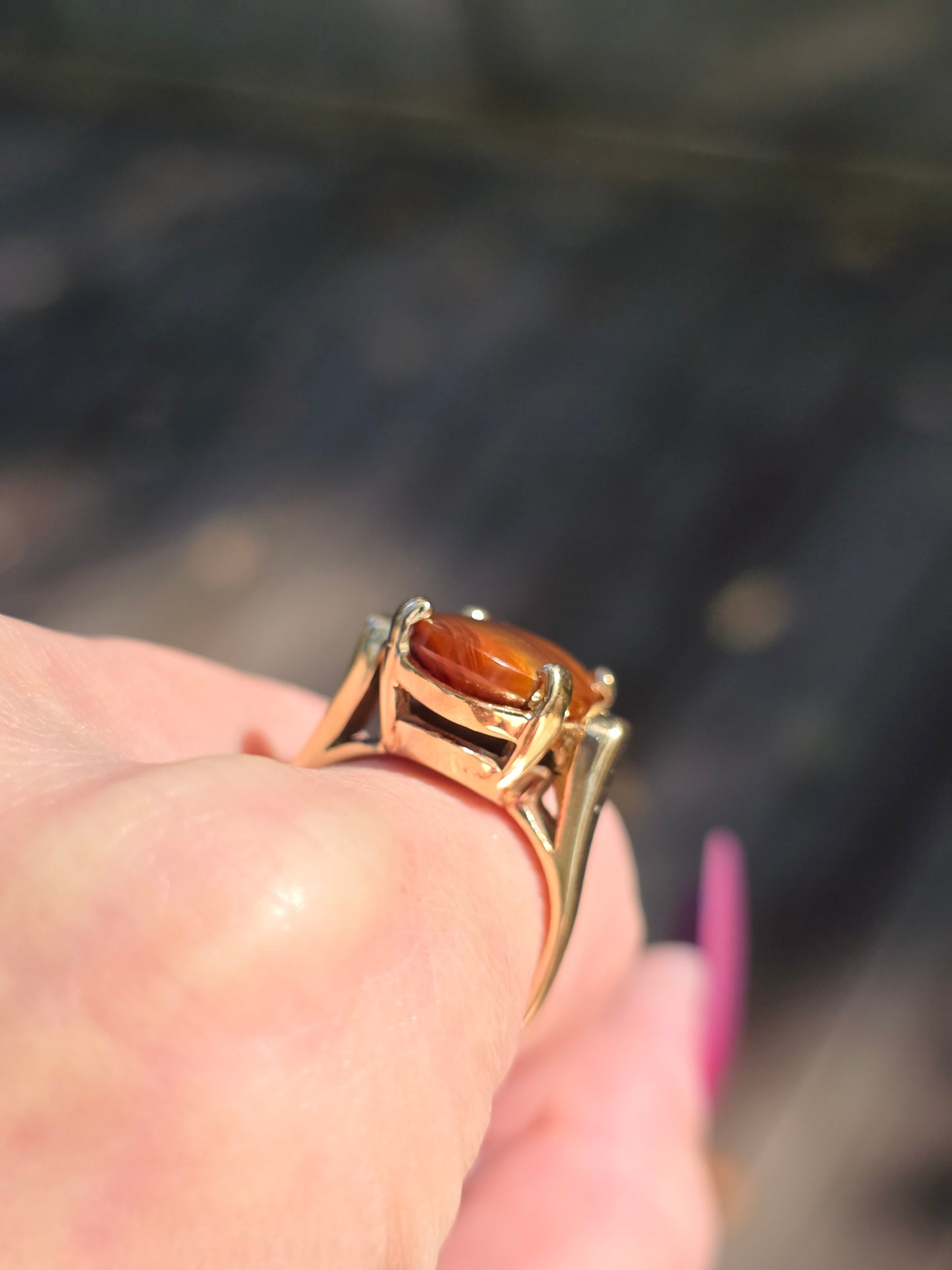 Gold ring with a large brown gemstone on a finger against a blurred background